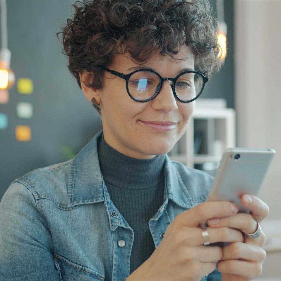 A smiling student in glasses typing a message on her phone